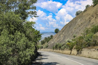 Dağların ve kırların arasındaki yol, kümülüs bulutlu mavi gökyüzü..
