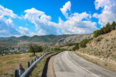 Dağların ve kırların arasındaki yol, kümülüs bulutlu mavi gökyüzü..