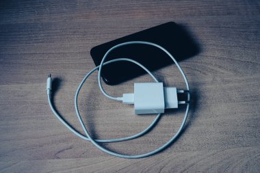 Grunge tarzı ahşap masadaki USB tip C kablo ve akıllı telefona sahip şarj cihazı