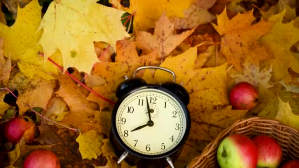 टोपलीवर सफरचंद आणि जमिनीवर रंगीत मॅपल पानांवर गजर घड्याळ. शरद ऋतू वेळ संकल्पना पॅनोरामा गती कॅमेरा व्हिडिओ . — स्टॉक व्हिडिओ