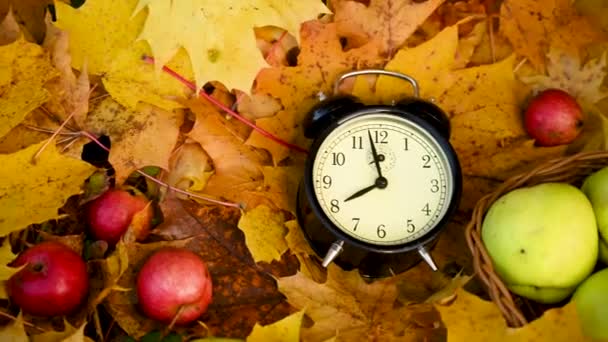 Manzanas en la cesta y despertador en hojas de arce de colores en el suelo. Otoño concepto de tiempo panorama movimiento cámara vídeo. — Vídeo de stock