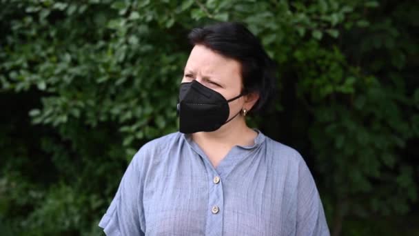 Nainen mustassa lääketieteellisessä naamiossa nostaa päänsä ja katsoo ylös. Musta hengityslaite. Pandemiakonseptin videomateriaali 4k — kuvapankkivideo