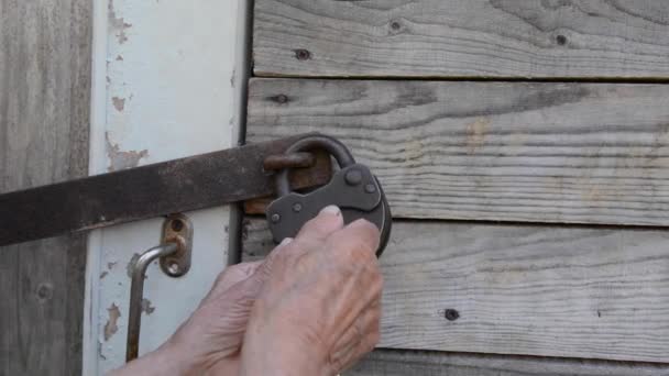 Een oudere vrouw sluit de deur. Een oud metalen hangslot. Houten huis. — Stockvideo