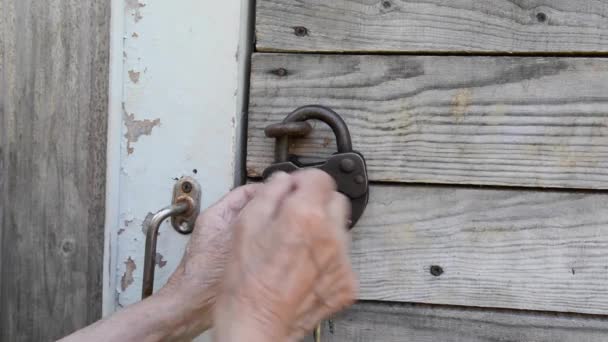 Mulher idosa abrir o velho cadeado de metal. Casa de madeira. — Vídeo de Stock