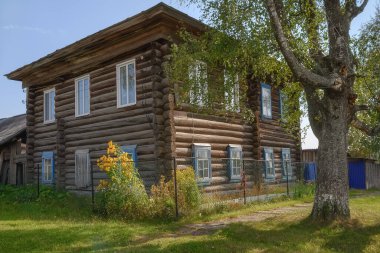İki katlı eski bir ahşap ev. Ön bahçesi ve çiçekleri var. Yazın geleneksel Rus tarzında. Yerleşim Nyrob (Kuzey Ural, Rusya). Yeşil çimenler ve yakınlarda uzun bir ağaç. 