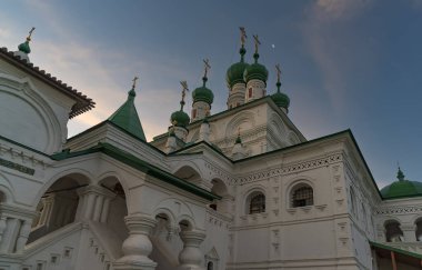 Bir yaz sabahı birçok yeşil kubbesi, yontulmuş taş elementleri, sütunları, kemerleri ve diğer mimari süslemeleri olan antik bir tapınağın üst kısmı. Sarı-mavi bulutlu gökyüzü. Rusya, Solikamsk 