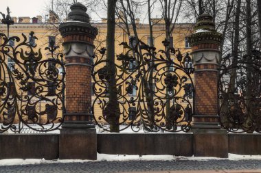 Kışın St. Petersburg 'daki Mikhailovsky Bahçesi' nin eski çardağı. Yaz Bahçesi sütunlarıyla dövülmüş şehir çitleri. Sanat detayı yakın plan. Bulutlu gökyüzü, yapraksız ağaçlar, yerde kar..