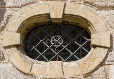 Doğal taştan yapılmış, desenli demir ızgaralı eski bir oval pencere. Doğal bir arka planda soyut bir şablon. İnşaat konsepti. Doğal dokular. Retro biçimi. 