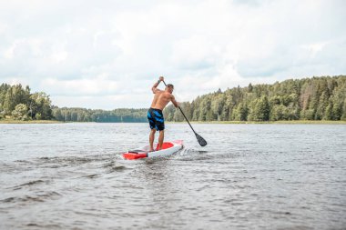 Paddling on a SUP board on a lake at sunny day. Stand up paddle boarding - awesome active outdoor recreation.