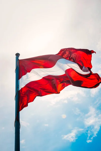Flag of the Republic of Latvia. Latvian flag waving in the wind against the sun