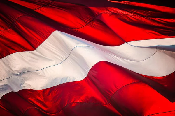 Close-up of Flag of the Republic of Latvia. Huge Latvian flag waving in the wind against the sun