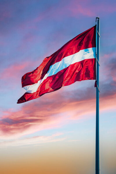 Flag of the Republic of Latvia. Latvian flag waving in the wind against the beautiful sunset