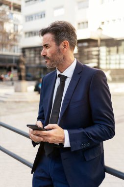 Olgun iş adamı sokakta akıllı telefon kullanıyor.