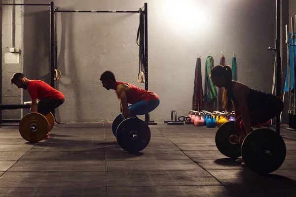 Three young adults lifting barbells. — Foto de Stock