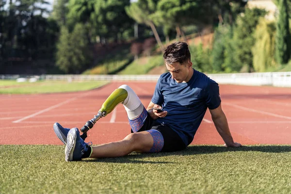 Disabled athlete sitting using phone — Stockfoto