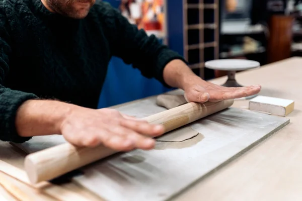 Stock photo of unrecognized person in apron working in pottery atelier and using clay.