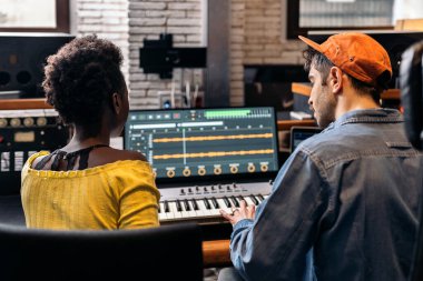 Siyahi bir kadının müzik stüdyosunda erkek yapımcıyla çalışırken çekilmiş resmi..