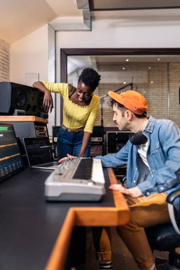 Siyahi bir kadının müzik stüdyosunda erkek yapımcıyla çalışırken çekilmiş resmi..