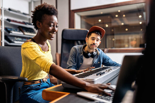 Stock photo of black woman playing electronic piano keyboard in music studio.