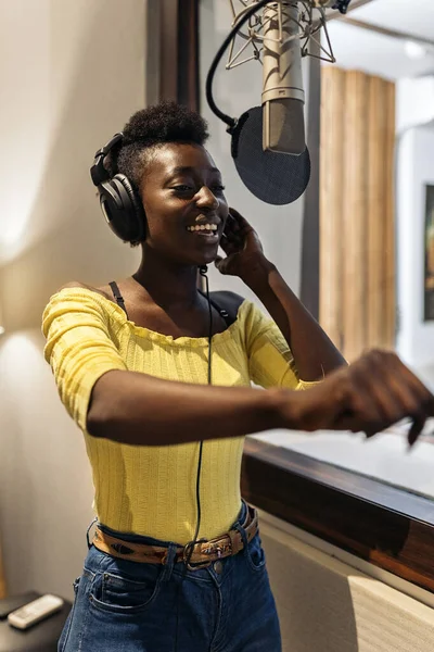 Stock photo of beautiful black woman singing and using microphone in music studio.