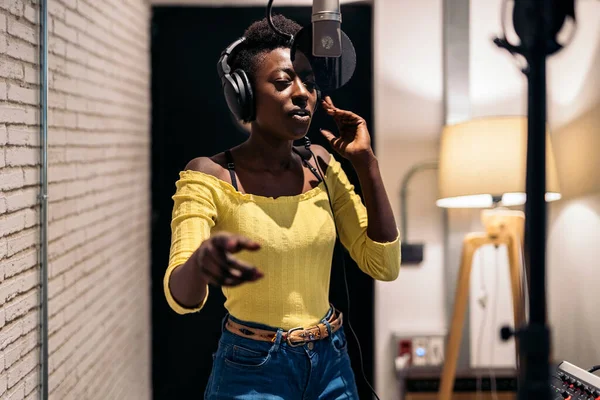Stock photo of beautiful black woman singing and using microphone in music studio.