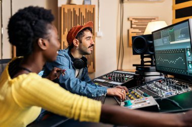 Genç müzik yapımcısıyla profesyonel müzik stüdyosunda çalışan mutlu zenci şarkıcının stok fotoğrafı..