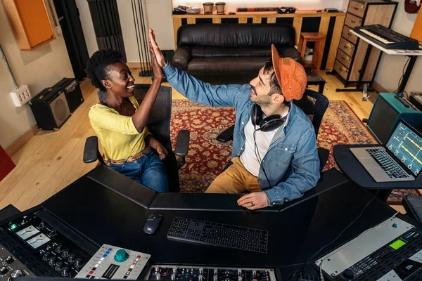 与年轻音乐制作人一起在专业音乐工作室工作的快乐黑人歌手的照片 — 图库照片