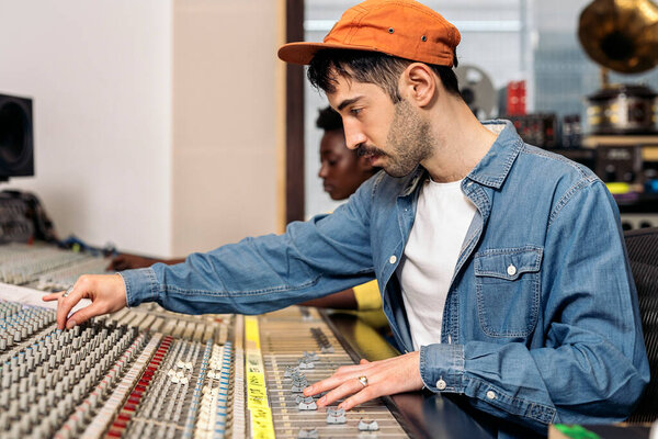 Stock photo of hipster man using panel control in professional music studio.