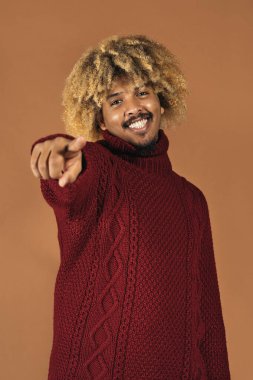 Stüdyoda gülümseyen afro adamın kahverengi arka planda kameraya bakarken çekilmiş resmi..