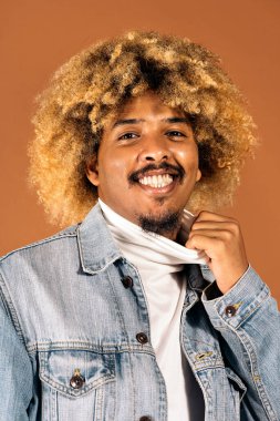 Stüdyoda kahverengi arka planda gülümseyen ve kameraya bakan neşeli afro adamın stok fotoğrafı..