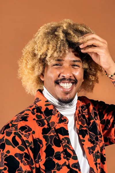 Stock photo of stylish afro man smiling and looking at camera in studio shot against brown background.