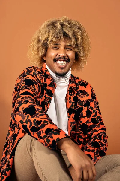 Stock photo of cheerful afro man smiling and looking at camera in studio shot against brown background.