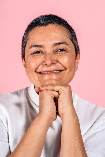 Stock photo of smiley woman with short grey hair having fun in studio shot against pink background.