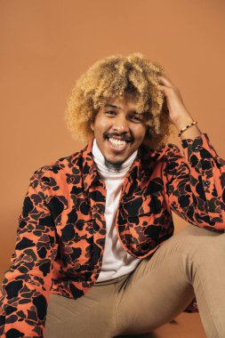 Stüdyoda kahverengi arka planda gülümseyen ve kameraya bakan havalı afro adamın stok fotoğrafı..