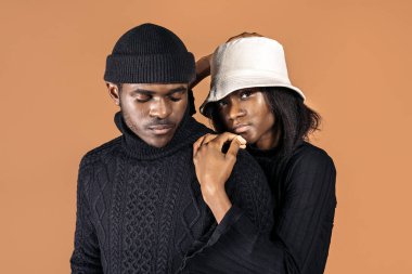 Siyahi bir adam ve kız arkadaşının sıradan bir şapka takıp stüdyoda kahverengi arka planda poz verirken çekilmiş resmi..
