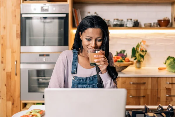 Happy Black Woman Drinking Juice Kitchen Home Using Computer — Foto de Stock