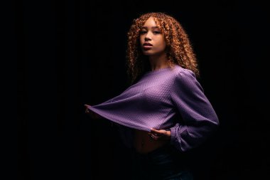 Stüdyoda kameraya bakan kıvırcık saçlı, etkileyici bir kadının stok fotoğrafı..