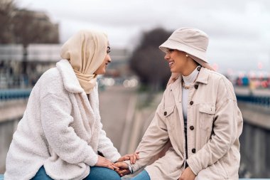 Cheerful young women wearing hijab talking and sitting in the city.