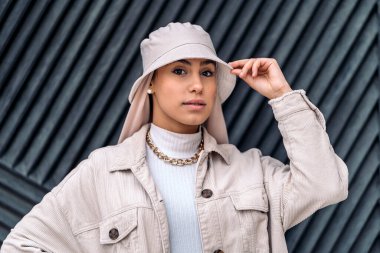 Başörtüsü takan, siyah duvara poz veren ve kameraya bakan gülümseyen müslüman kadın..