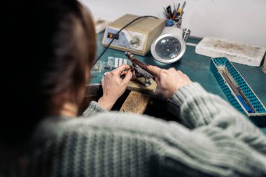 Unrecognized craftswoman working jewelry workshop using tools.