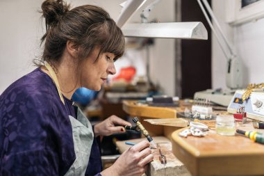 Concentrated adult woman using blowtorch in jewelry workshop.