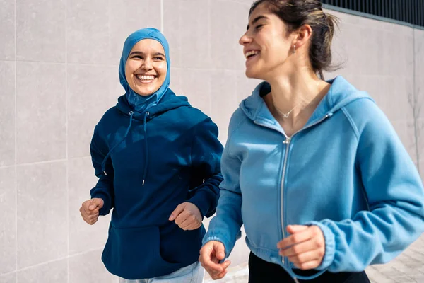 Multicultural female friends wearing sports clothes running in the city and having fun.