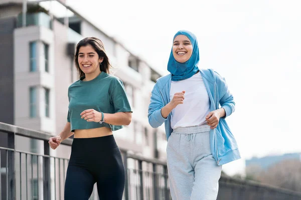 Cheerful muslim woman wearing hijab running in the street with her friend and having fun.