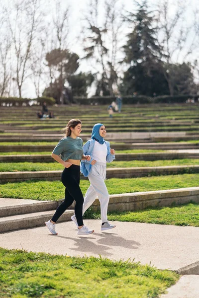 Cheerful muslim woman wearing hijab running in the park with her friend and having fun.