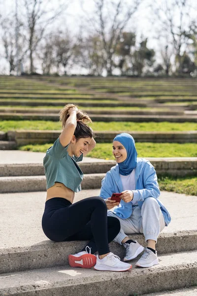 Happy Muslim Girl Her Friend Sitting Park Talking Using Mobile — Fotografia de Stock