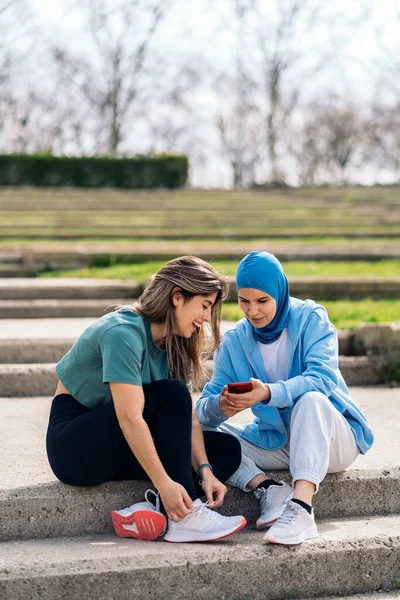 Happy Muslim Girl Her Friend Sitting Park Talking Using Mobile — Fotografia de Stock