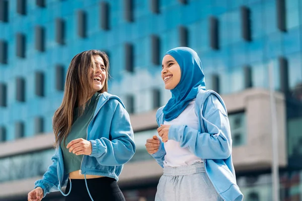 Cheerful muslim woman wearing hijab running in the street with her friend and having fun.