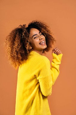 Beautiful black woman with curly hair smiling and having fun in studio shot against brown background.
