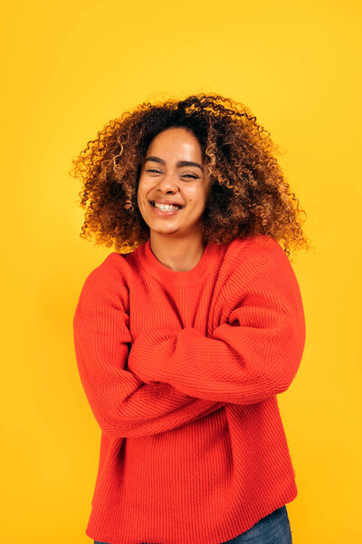 Beautiful black woman with curly hair smiling and looking at camera in studio shot against yellow background.