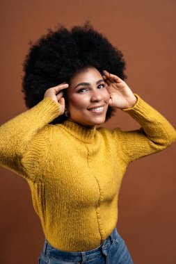 Smiley afro girl having fun in studio shot against brown background.